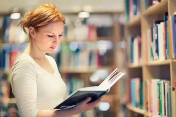 Ung kvinna läser bok i bibliotek