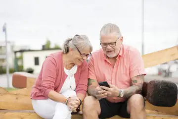 Äldre kvinna och man sitter och tittar i en mobiltelefon