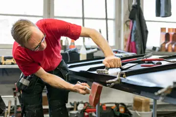 En plåtslagare i röd tröja står och arbetar med ett stycke plåt.