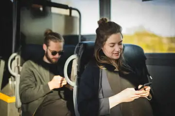 Man och kvinna sitter på varsitt säte i buss och kollar på mobilen