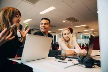 Tre ungdomar, två tjejer och en kille, sitter tillsammans och studerar vid datorskärm