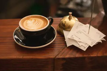En dyr kopp kaffe på en hotelldisk med guldklocka och kvitton.