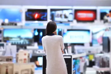En kvinnlig kund står och tittar på olika tv-skärmar i en elektronikbutik