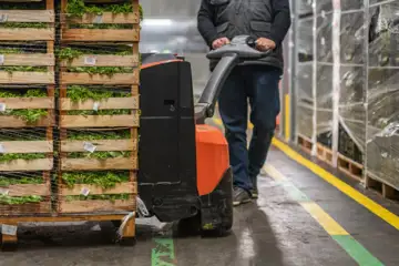 Person flyttar pallar med grönsaker på ett lager