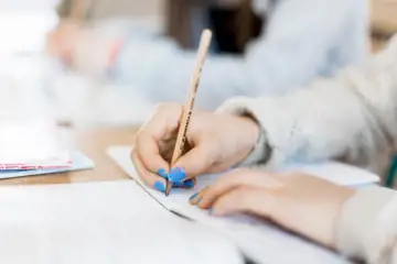 Hand med framträdande blått nagellack som som håller i penna och skriver på papper