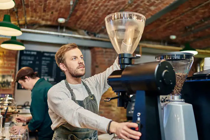 Ung man brygger kaffe bakom disken på ett kafé