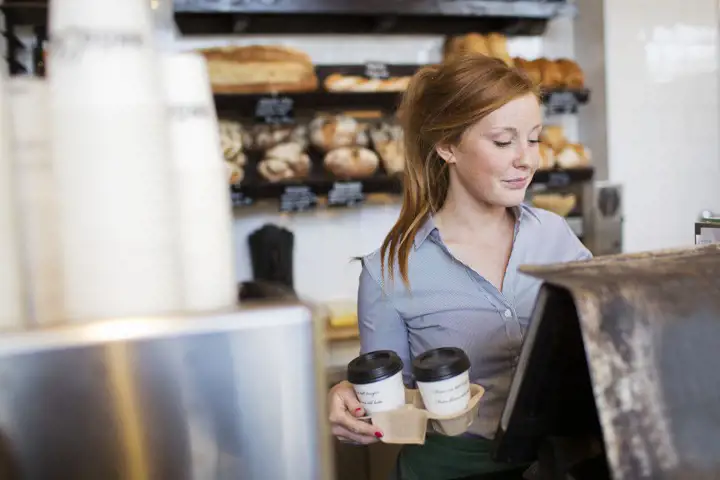Ung kvinna står bakom disken på ett kafé