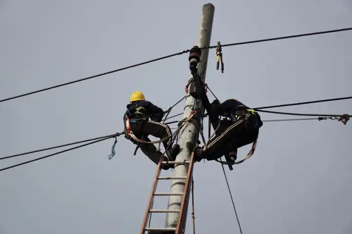 Two men climbing a pole with electrical wires