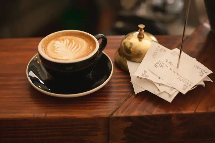 En dyr kopp kaffe på en hotelldisk med guldklocka och kvitton.