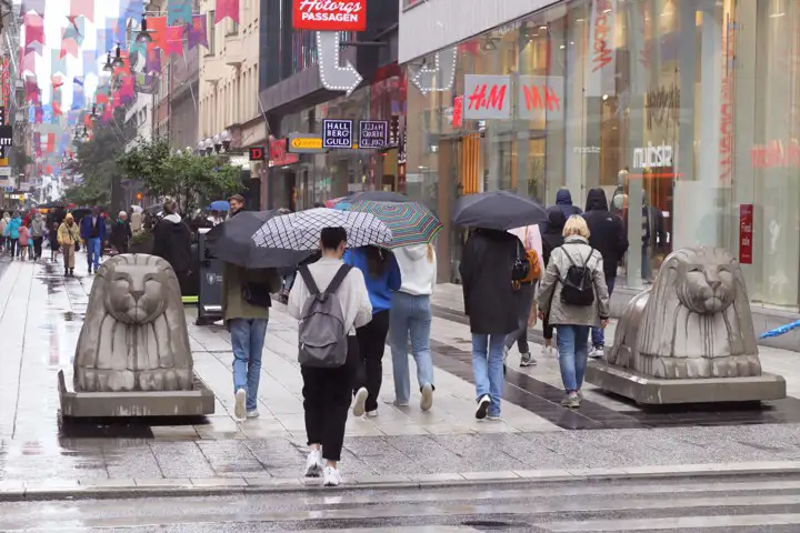 Människor går med paraplyer på ett regnigt Drottninggatan i Stockholm